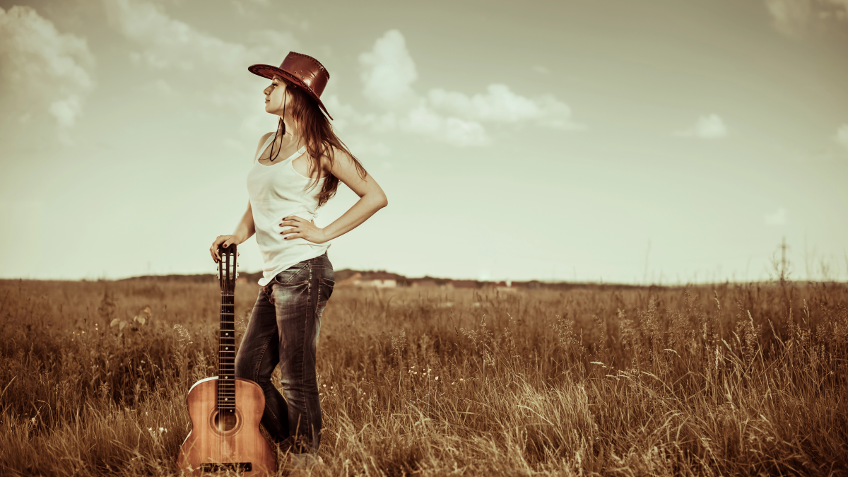 A girl standing in a field holding a guitar
