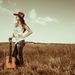 A girl standing in a field holding a guitar