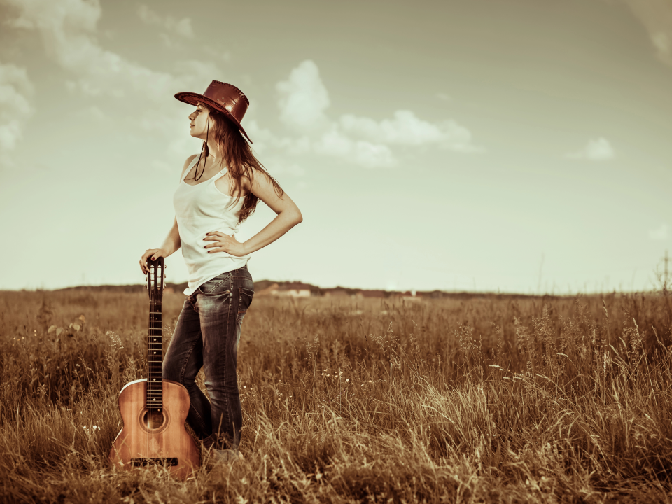 A girl standing in a field holding a guitar